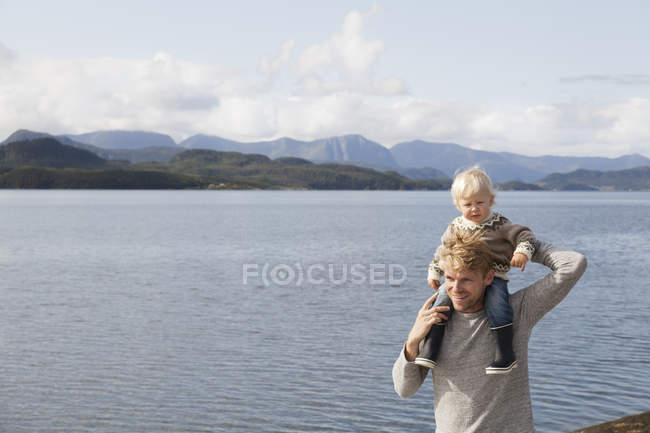 Man carrying son on shoulders by fjord, Aure, More og Romsdal, Norway — Stock Photo