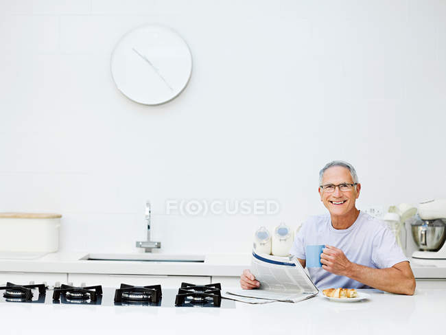 Uomo anziano che fa colazione e legge giornali — Foto stock