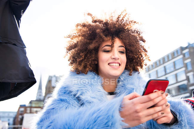 Porträt einer Frau mit Afro, die auf ihr Smartphone blickt — Stockfoto