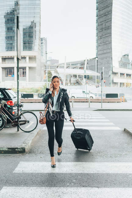 Donna che cammina con valigia a ruote e parla su smartphone — Foto stock