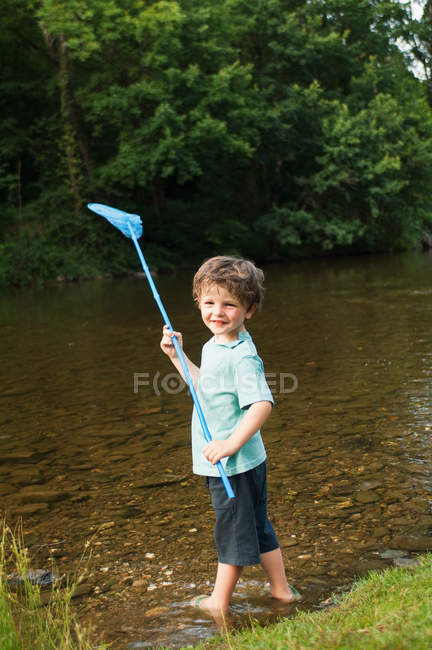 Boy holding fishing net by river — Stock Photo
