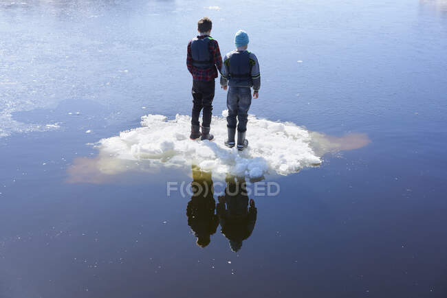 Dos chicos parados en el hielo, en el lago, vista trasera - foto de stock