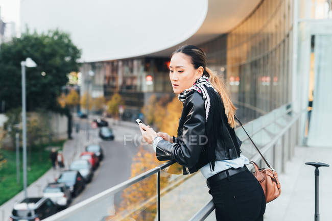 Жінка спирається на перила, тримаючи смартфон — стокове фото
