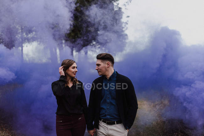 Jovem casal de mãos dadas pela nuvem de fumaça azul — Fotografia de Stock