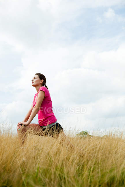 Jovem mulher se esticando no campo — Fotografia de Stock