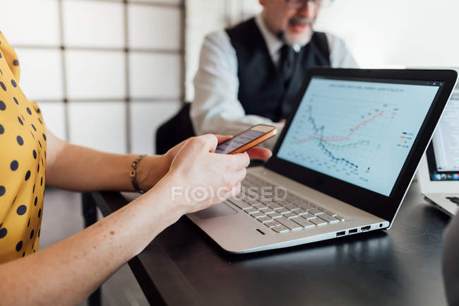 Donna che utilizza smartphone e laptop alla scrivania dell'ufficio — Foto stock
