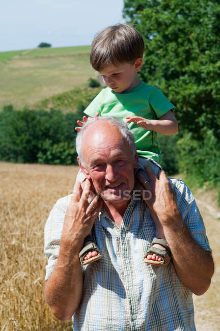 Grandfather carrying grandson on shoulders, portrait — Stock Photo