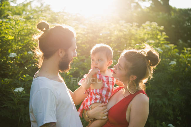 Couple with baby girl in sunlit garden — Stock Photo