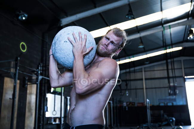 Man exercising in gymnasium, using atlas stone — Stock Photo