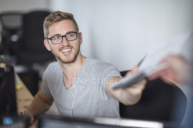Young man handing paperwork to colleague in office — Stock Photo