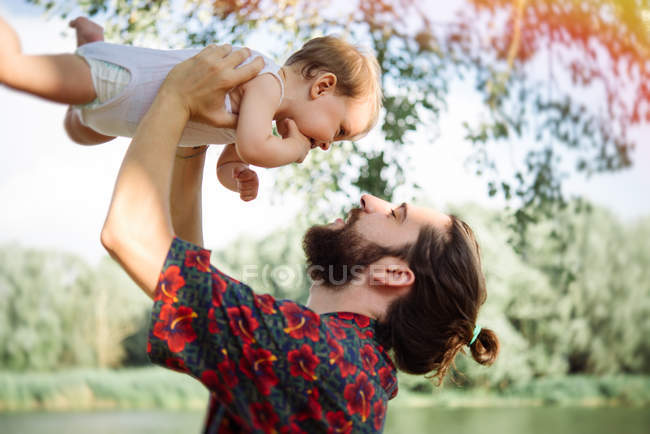 Vista lateral do homem levantando bebê menina por lago, Arezzo, Toscana, Itália — Fotografia de Stock