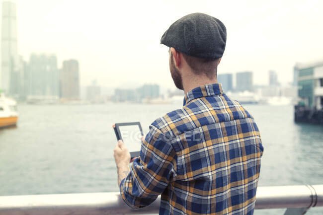 Mann mit digitalem Tablet blickt weg auf Hafenblick, Rückansicht, Hongkong, China, Ostasien — Stockfoto