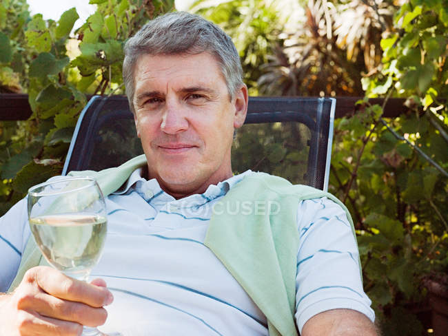 Человек держит стакан белого вина в саду — стоковое фото