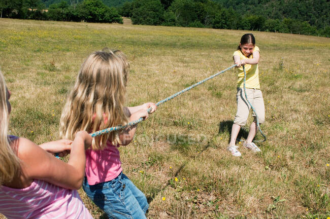 Três meninas jogando rebocador de guerra no campo — Fotografia de Stock