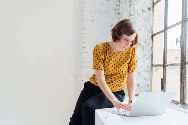 Geschäftsfrau sitzt auf Fensterbank und benutzt Laptop — Stockfoto