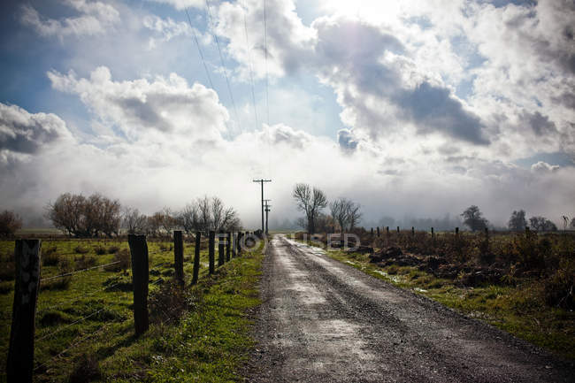 Сельская дорога с забором и облаками в небе — стоковое фото