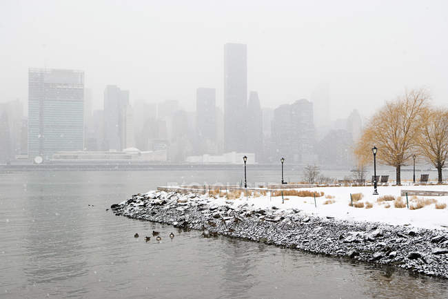 Verschneiter Park, Fluss und Wolkenkratzer an der Skyline im Winter, New York, USA — Stockfoto