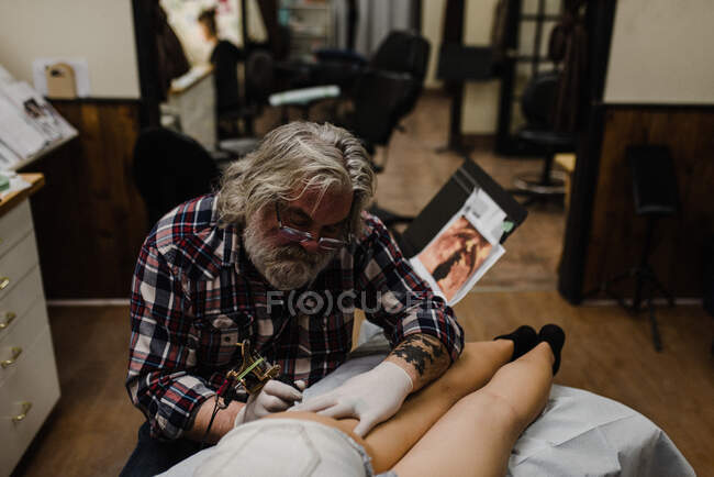 Tattooist tattooing young woman's thigh — Stock Photo