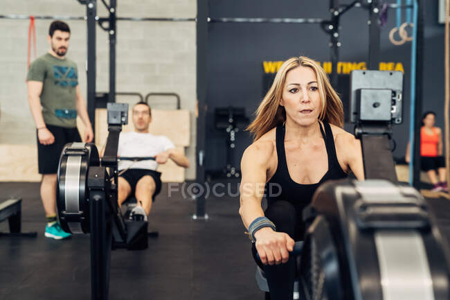 Mujer usando máquina de remo en el gimnasio - foto de stock