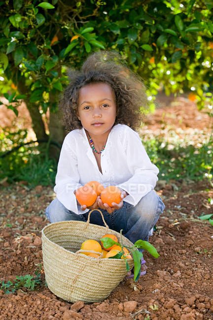 Девушка с корзиной апельсинов смотрит в камеру — стоковое фото