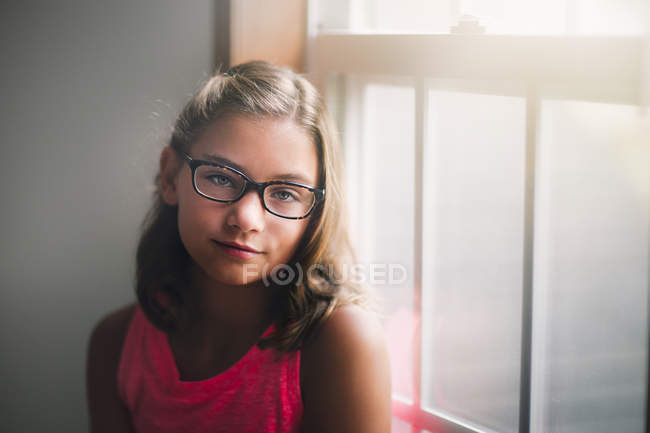 Retrato de menina em óculos de pé ao lado da janela — Fotografia de Stock