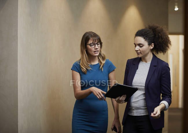 Femmes d'affaires marchant et regardant la tablette numérique dans le couloir de bureau — Photo de stock