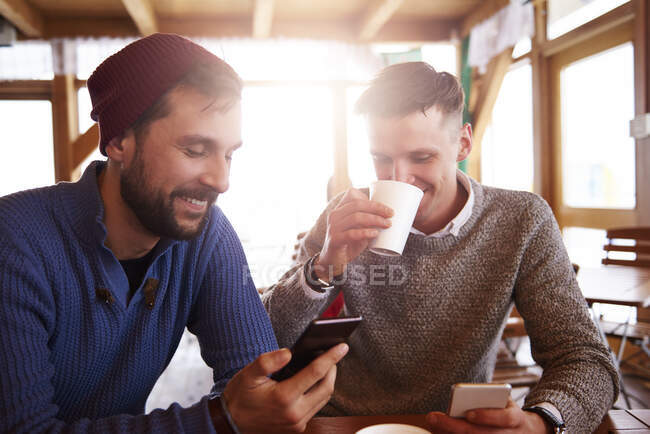 Hombres jóvenes sonriendo sobre mensajes de texto en teléfonos móviles - foto de stock