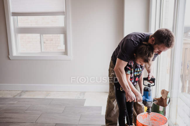 Padre e hija mezclando cemento en cubo con mezclador de mano - foto de stock