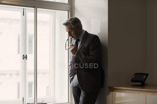 Homme d'affaires au bureau appuyé contre le mur et tenant des lunettes — Photo de stock