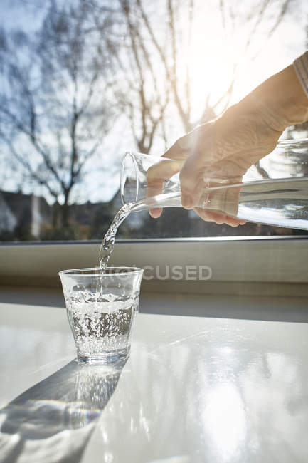 Woman pouring water from transparent decanter into glass — Stock Photo