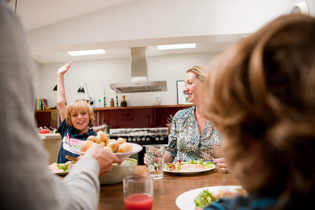 Familie am Esstisch, Sohn hebt Arm und bittet um mehr Essen — Stockfoto