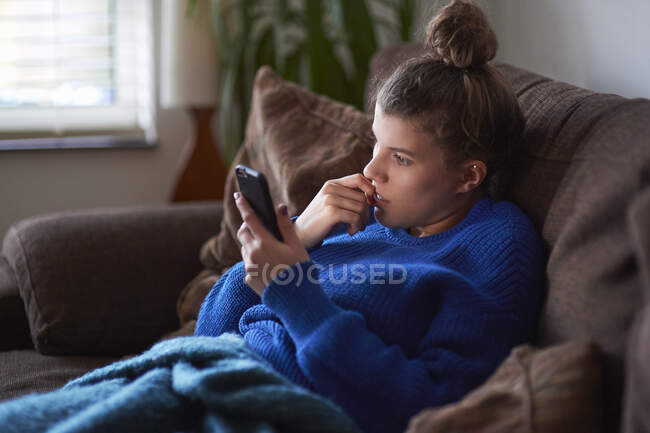 Jeune femme sur canapé regardant smartphone — Photo de stock