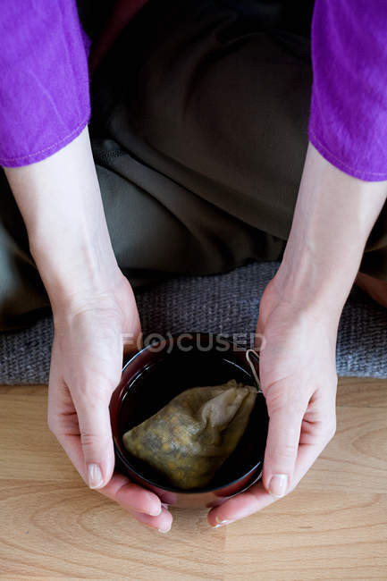 Обрезанное изображение женщины, берущей чашку травяного чая с пола — стоковое фото