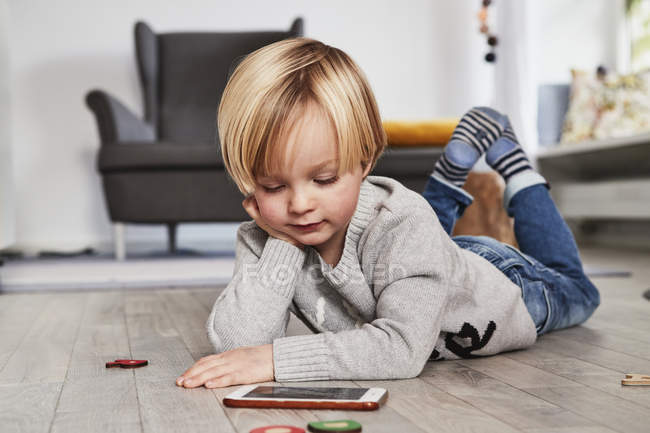 Мальчик лежит на полу и смотрит на смартфон — стоковое фото