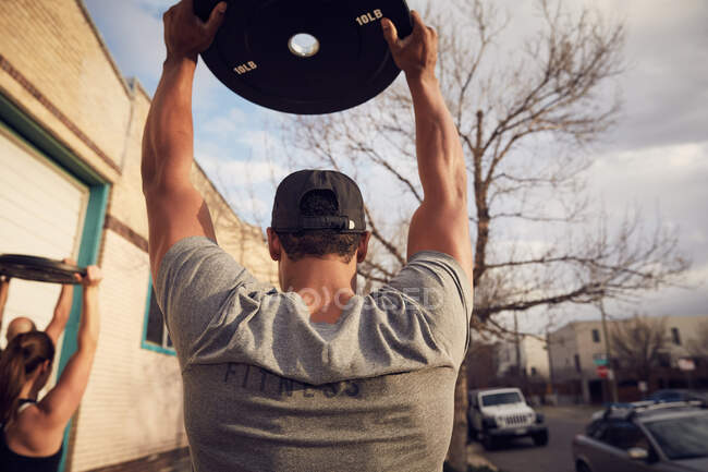 Rear view of mid adult man with arms raised carrying weights equipment — Stock Photo