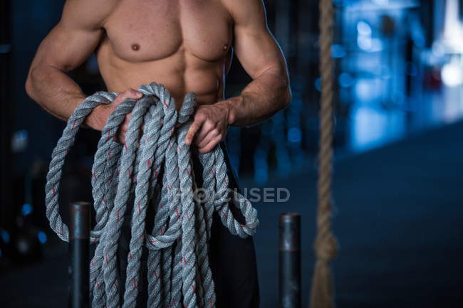 Мужчина тренируется в гимназии, держит верёвку, готовится к тренировкам на санях, середина секции — стоковое фото