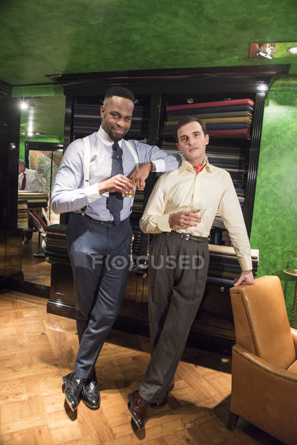 Two stylish tailors holding whiskey in tailors shop — Stock Photo