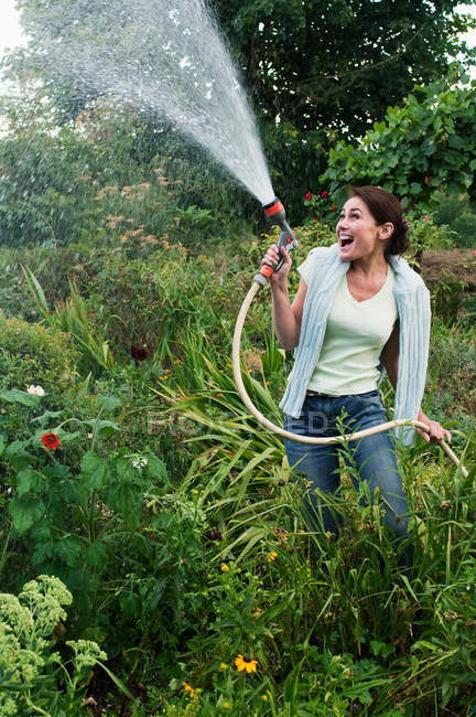 Улыбающаяся женщина обрызгивает сад шлангом — стоковое фото