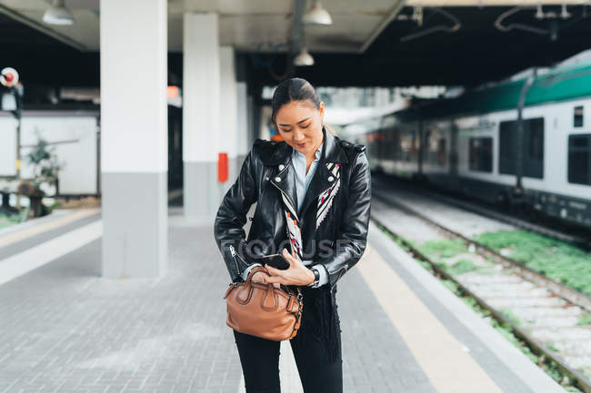 Donna con smartphone in piedi vicino alla piattaforma ferroviaria — Foto stock