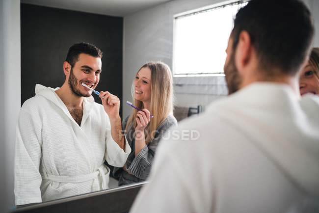 Imagem espelhada de casal escovando dentes no banheiro — Fotografia de Stock