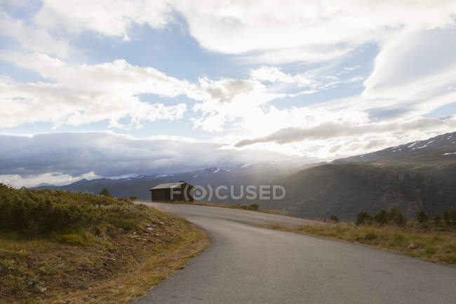 Estrada rural iluminada pelo sol na paisagem montanhosa, Parque Nacional Jotunheimen, Lom, Oppland, Noruega — Fotografia de Stock