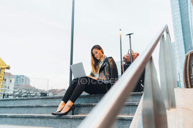 Empresaria sentada al aire libre en escalones y usando laptop - foto de stock