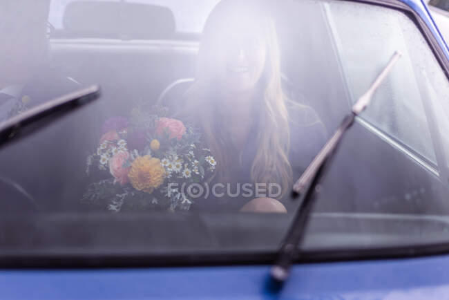 Young woman in car with flower bouquet, driving from wedding — Stock Photo
