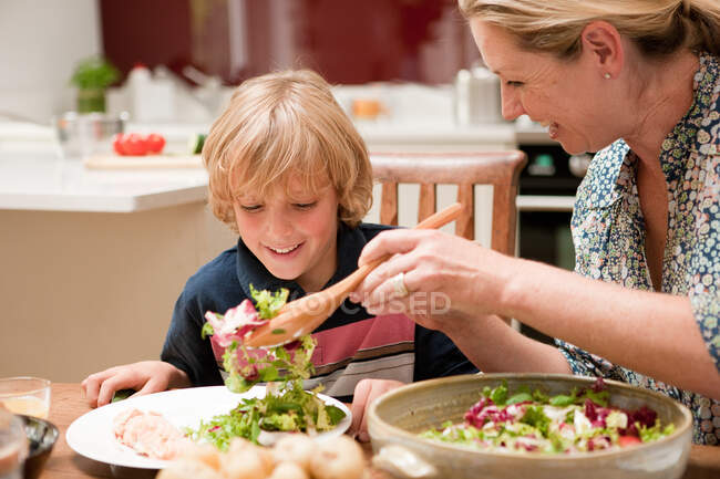 Мать подает салат сыну за обеденным столом — стоковое фото