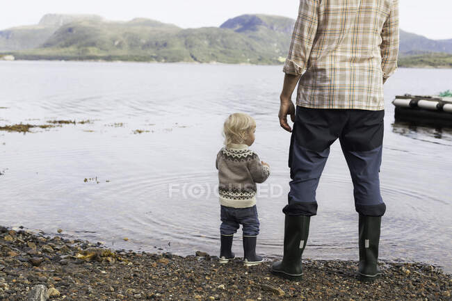 Niño y padre en el borde del fiordo mirando hacia fuera, Aure, Más og Romsdal, Noruega - foto de stock