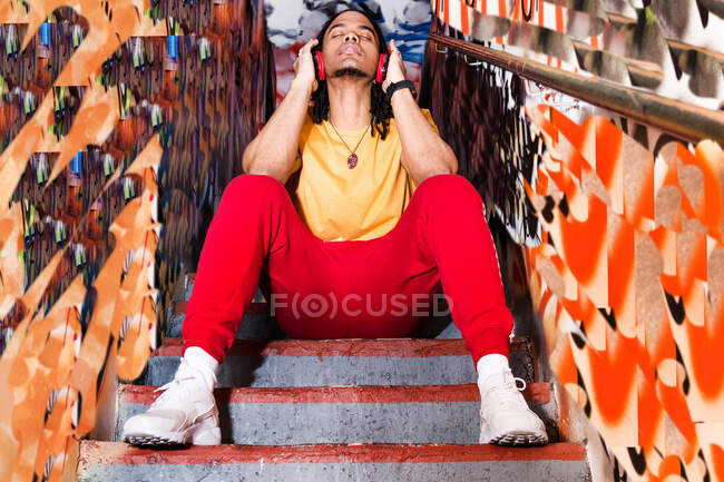 Молодий чоловік сидить на сходах, носить навушники, слухає музику, низький кут зору — стокове фото