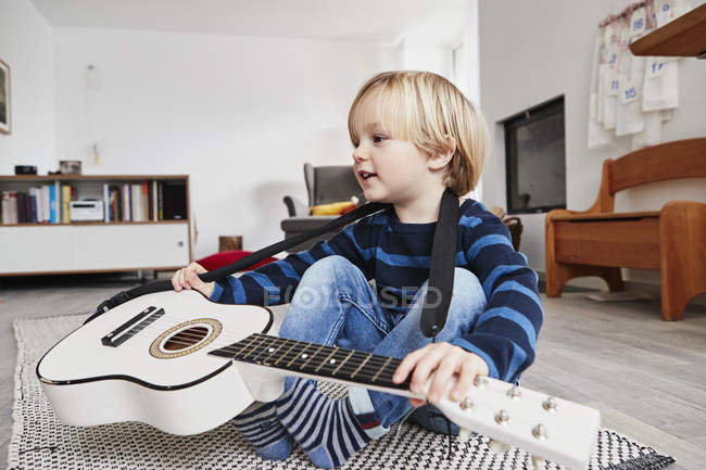 Jovem sentado com guitarra em torno do pescoço — Fotografia de Stock