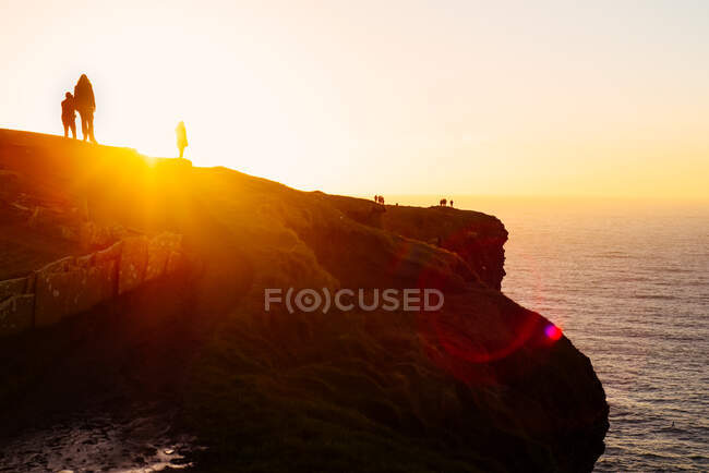 Personnes au sommet d'une falaise regardant le coucher du soleil, Liscannor, Clare, Irlande — Photo de stock