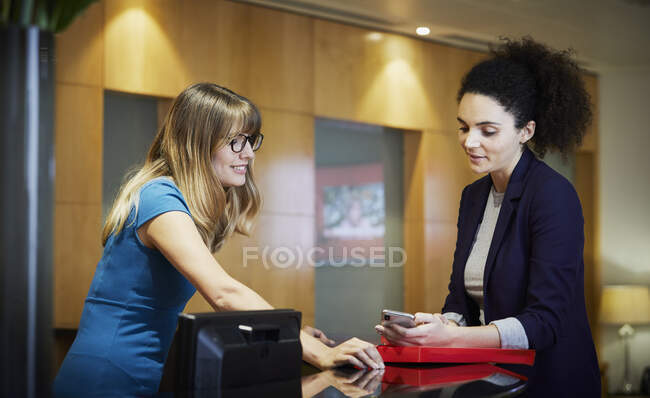 Zwei Geschäftsfrauen schauen in Büro-Rezeption aufs Smartphone — Stockfoto