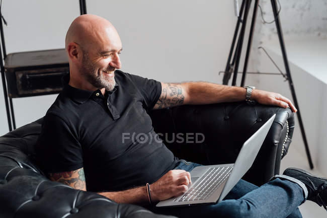 Homem em poltrona usando laptop e sorrindo — Fotografia de Stock